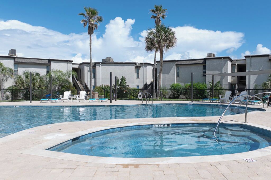 Una piscina con sillas de descanso y palmeras, rodeada de un edificio de diseño moderno.