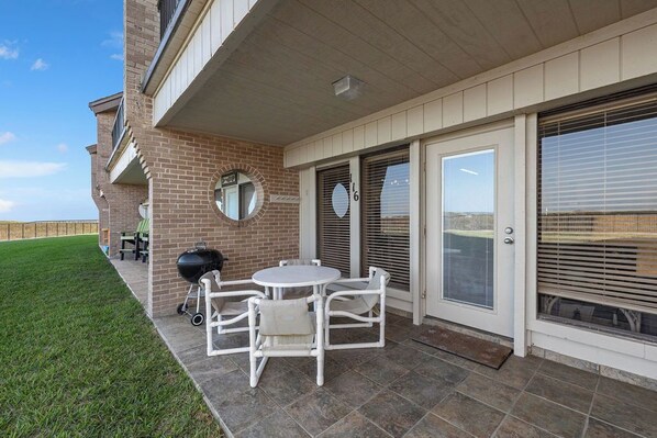 A patio with a grill, white chairs, and a round table. - Beachfront by South Padre Resort Rentals (South Padre Island)