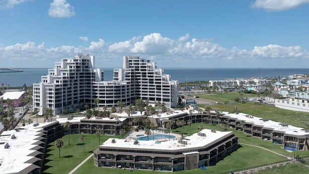 Un hotel moderno con varias construcciones, un área de piscina central y vista al océano.