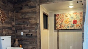 A bathroom with a wooden floor, a toilet, a sink, and a shower area. - The willow boho tent (Irwin)