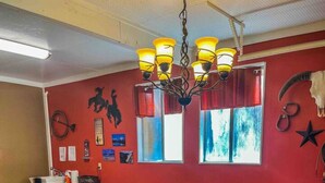 A dining area with a glass-top table, wooden chairs, a chandelier, and red walls with various decorations. - The willow boho tent (Irwin)