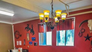 A dining area with a glass-top table, wooden chairs, a chandelier, and red walls with various decorations. - The willow boho tent (Irwin)