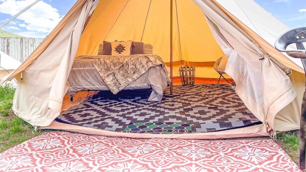 A tent with a bed inside, a patterned rug on the floor, and a welcome mat outside. - The willow boho tent (Irwin)