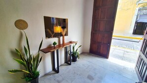 A hallway with a wooden bench, potted plants, a decorative wall piece, and a large wooden door. - Economic Master double Queen-size-room in Downtown Mérida (Mérida)