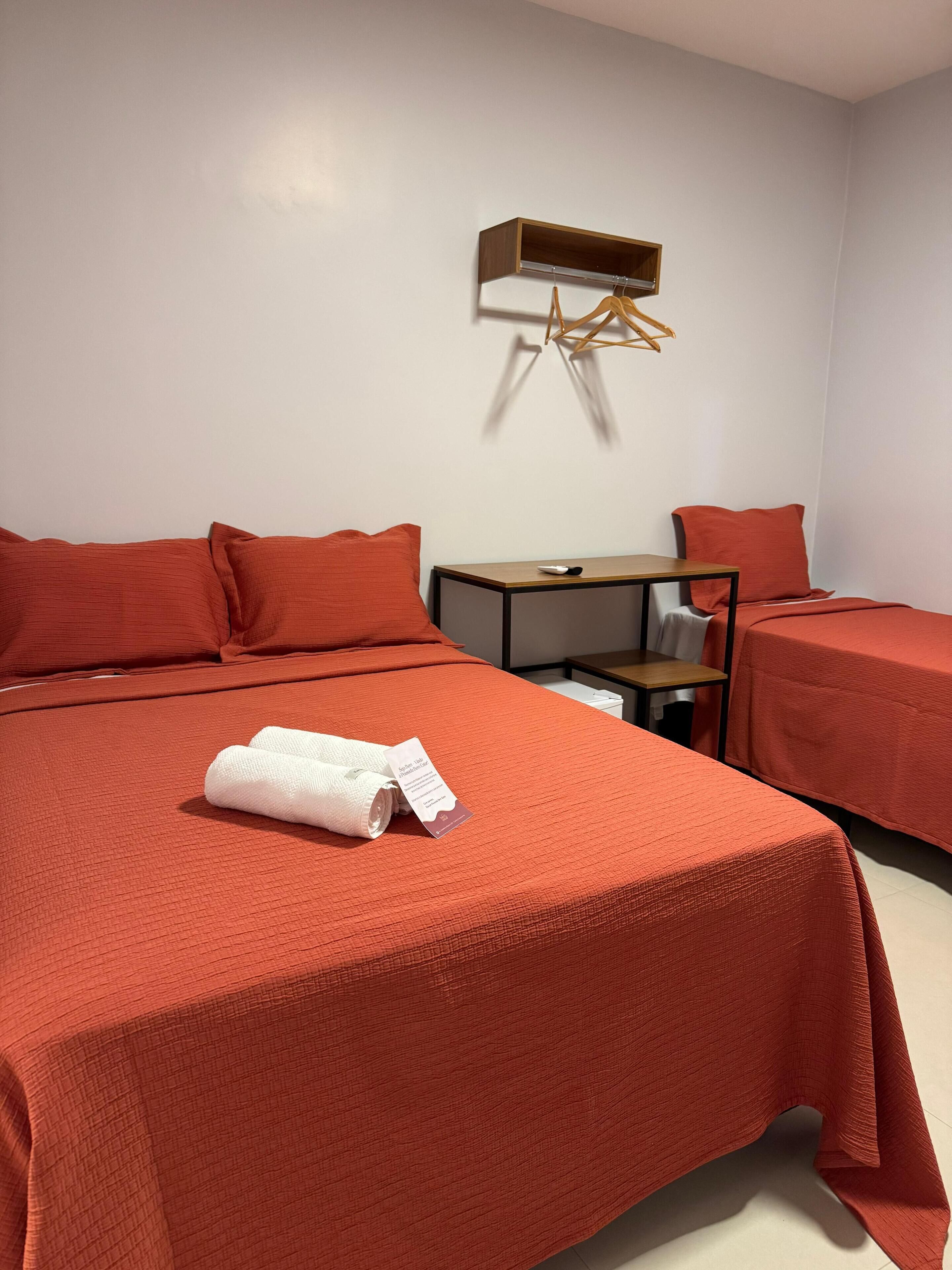 A hotel room with two beds, a wooden nightstand, a small table, and a wall-mounted air conditioning unit.