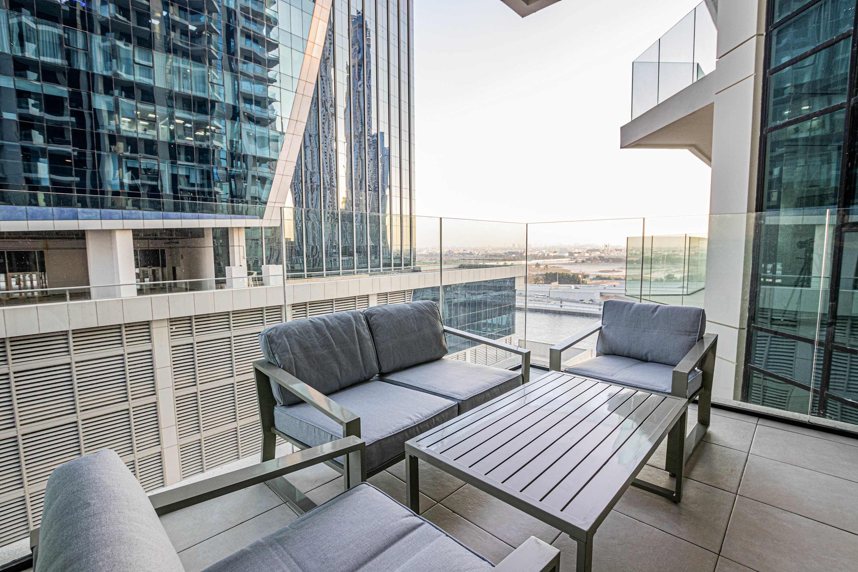 Ein moderner Balkon mit einer Couch, einem Tisch und Blick auf eine Stadtansicht.