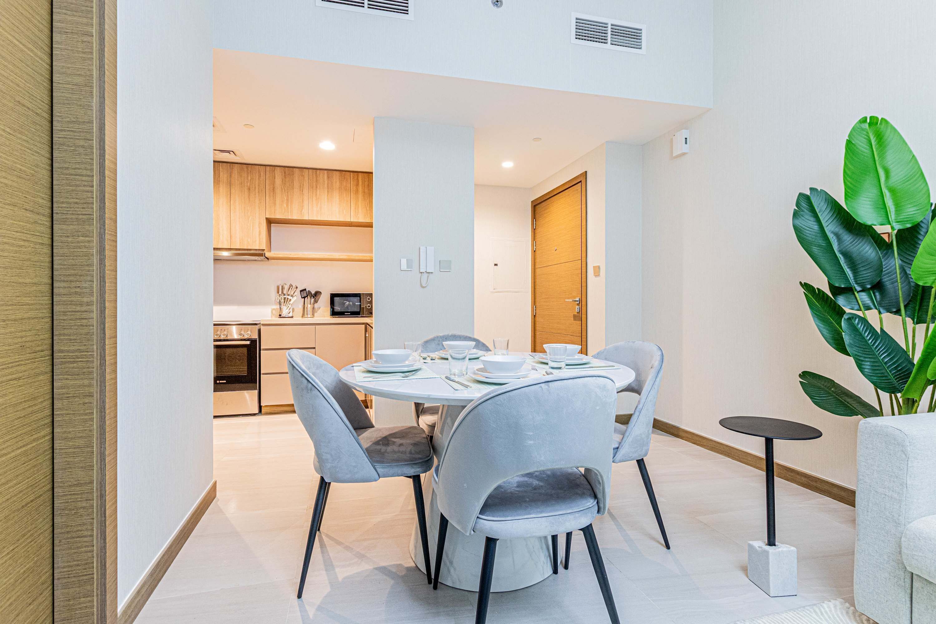 Uma área de jantar moderna com uma mesa redonda, cadeiras estofadas cinzentas e uma pequena mesa lateral.