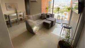 A modern living room with a sectional sofa, a dining table with chairs, and a balcony with potted plants.