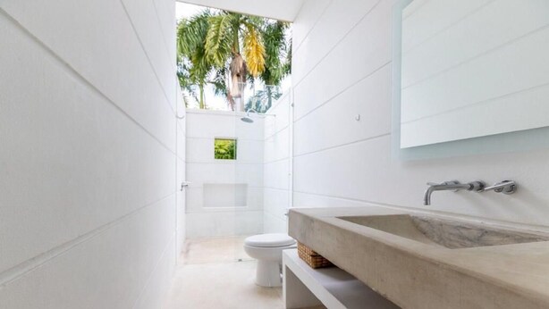 A modern bathroom with a large sink, a toilet, and a small window with a view of palm trees. - Yeguas Z26 by Wynwood House (Anapoima)