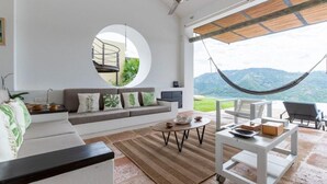 A spacious living area with a large window, a hammock, and a view of the mountains. - Yeguas Z26 by Wynwood House (Anapoima)