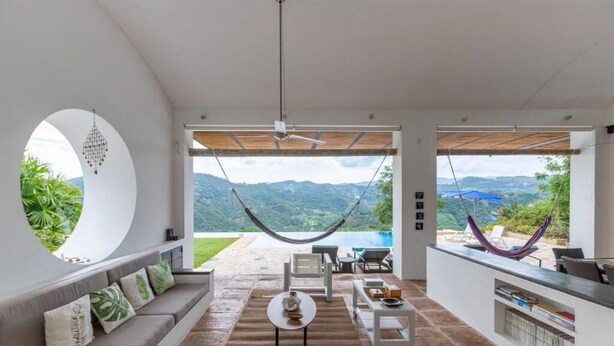 A spacious living area with a large window, a hammock, and a view of mountains. - Yeguas Z26 by Wynwood House (Anapoima)