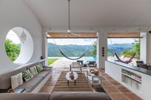 A spacious living area with a large window, a hammock, and a view of mountains. - Yeguas Z26 by Wynwood House (Anapoima)