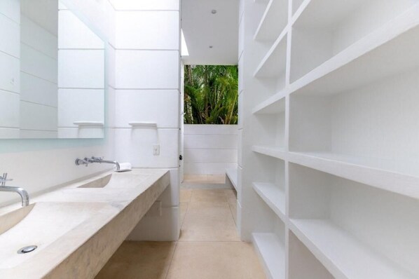 A modern bathroom with white fixtures, a large mirror, and a view of greenery through a window.