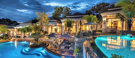 A resort with a large swimming pool, outdoor seating, and well-lit buildings.