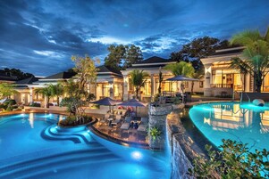 Un resort con una amplia piscina, mobiliario exterior y edificios bien iluminados.