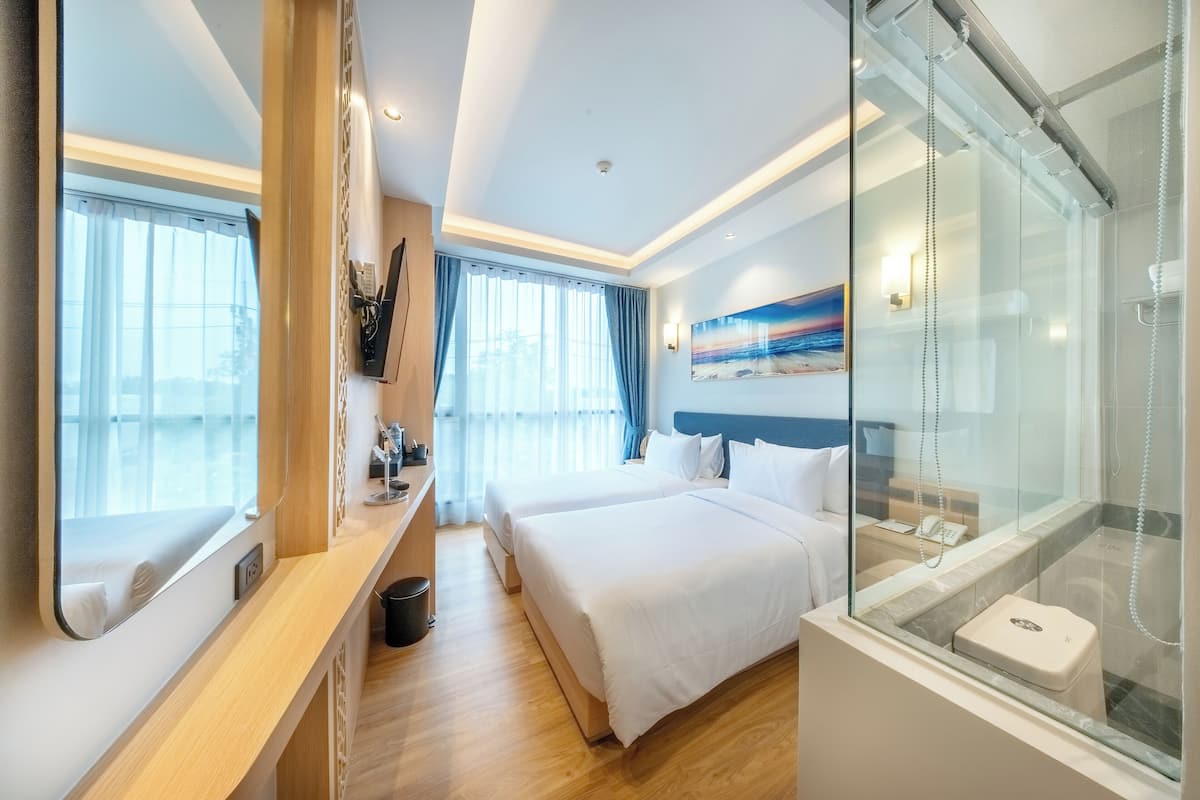 Une chambre d’hôtel avec un grand lit, une salle de bain séparée dotée d’une douche en verre, et une vue sur la mer depuis la fenêtre.