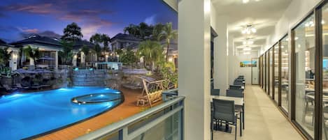 A hotel balcony with a pool, outdoor seating, and a view of neighboring houses.