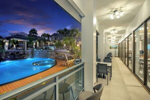 Un balcon d’hôtel avec une piscine, un espace salon extérieur et une vue sur les maisons voisines.