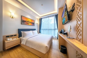 Een moderne hotelkamer met een groot bed, een nachtkastje met telefoon, een tv aan de muur en een raam met gordijnen.