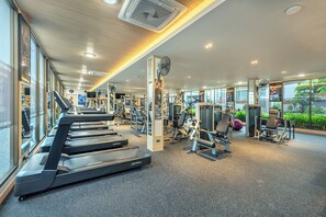 A modern gym with treadmills, weight machines, and a large window offering a view of greenery. - A.z.sunrise Resort And Fitness Club (Choeng Thale)