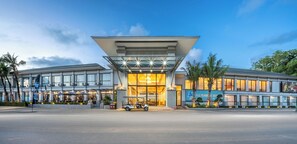 A modern hotel with a glass facade, a golf cart in front, and palm trees around. - A.z.sunrise Resort And Fitness Club (Choeng Thale)