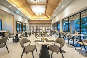Een ruime eethoek met ronde tafels, moderne stoelen en grote ramen met uitzicht op het omliggende landschap.