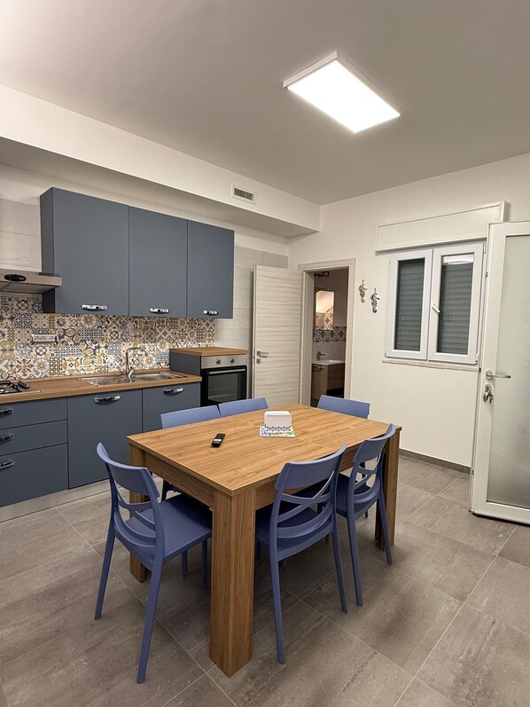 A modern kitchen with a wooden dining table and blue chairs, a tiled backsplash, and a white door with a window. - Tourist Location Le Vele I Relax with the whole family in this accommodation (San Pietro In Bevagna)