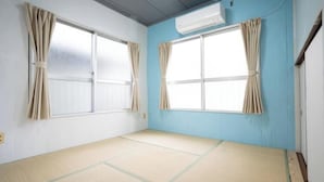 A room with tatami flooring, two windows with curtains, and an air conditioning unit on the wall.