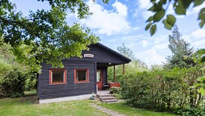 A small, dark wooden cabin with a porch, surrounded by lush greenery. - 3 bedroom lovely home in Sydals (Sydals)