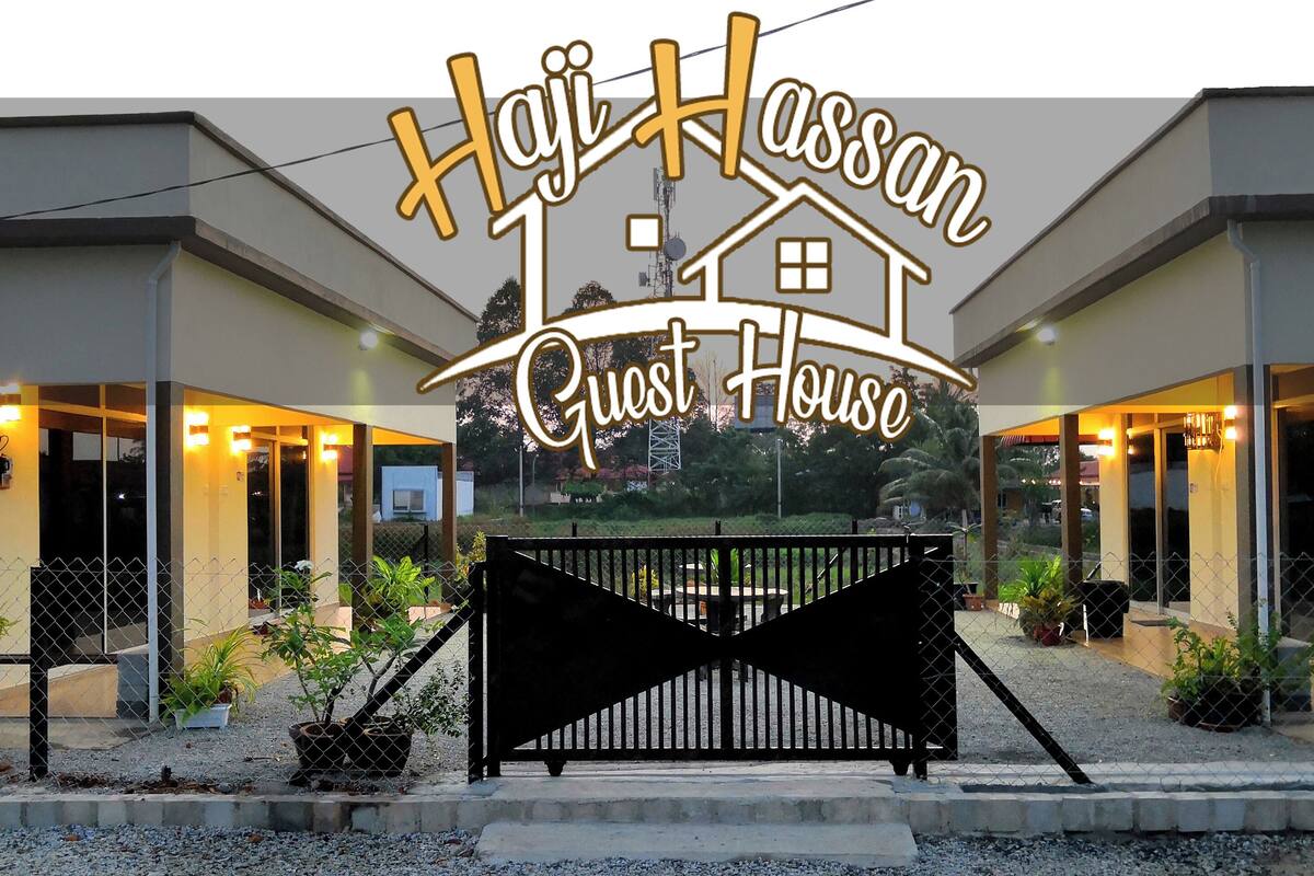 Ein Gästehaus mit einem Schild, auf dem 'Haji Hassan Guest House' steht, und einem schwarzen Tor im Vordergrund.