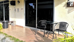 An outdoor patio with a table and chairs, a trash bin, and a sliding glass door leading to a garden. - Haji Hassan Guest House (Langkawi)
