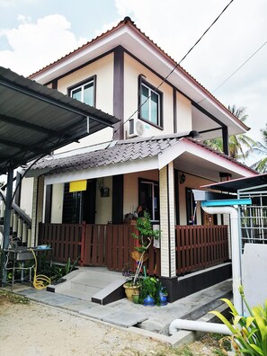 A two-story house with a covered porch, a small garden area with potted plants, and a visible staircase leading to the entrance.