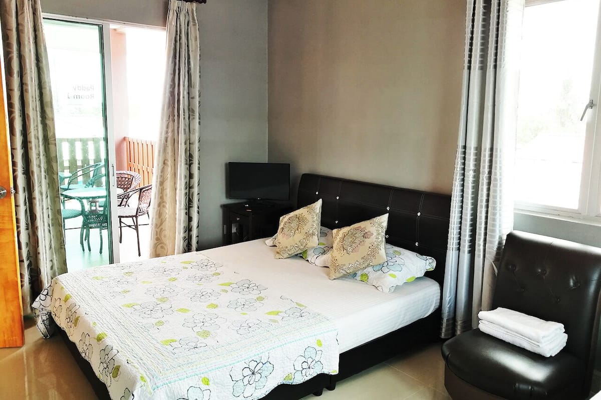 Ein Schlafzimmer mit Bett, Fernseher, Stuhl und einem Balkon mit Tisch und Stühlen.