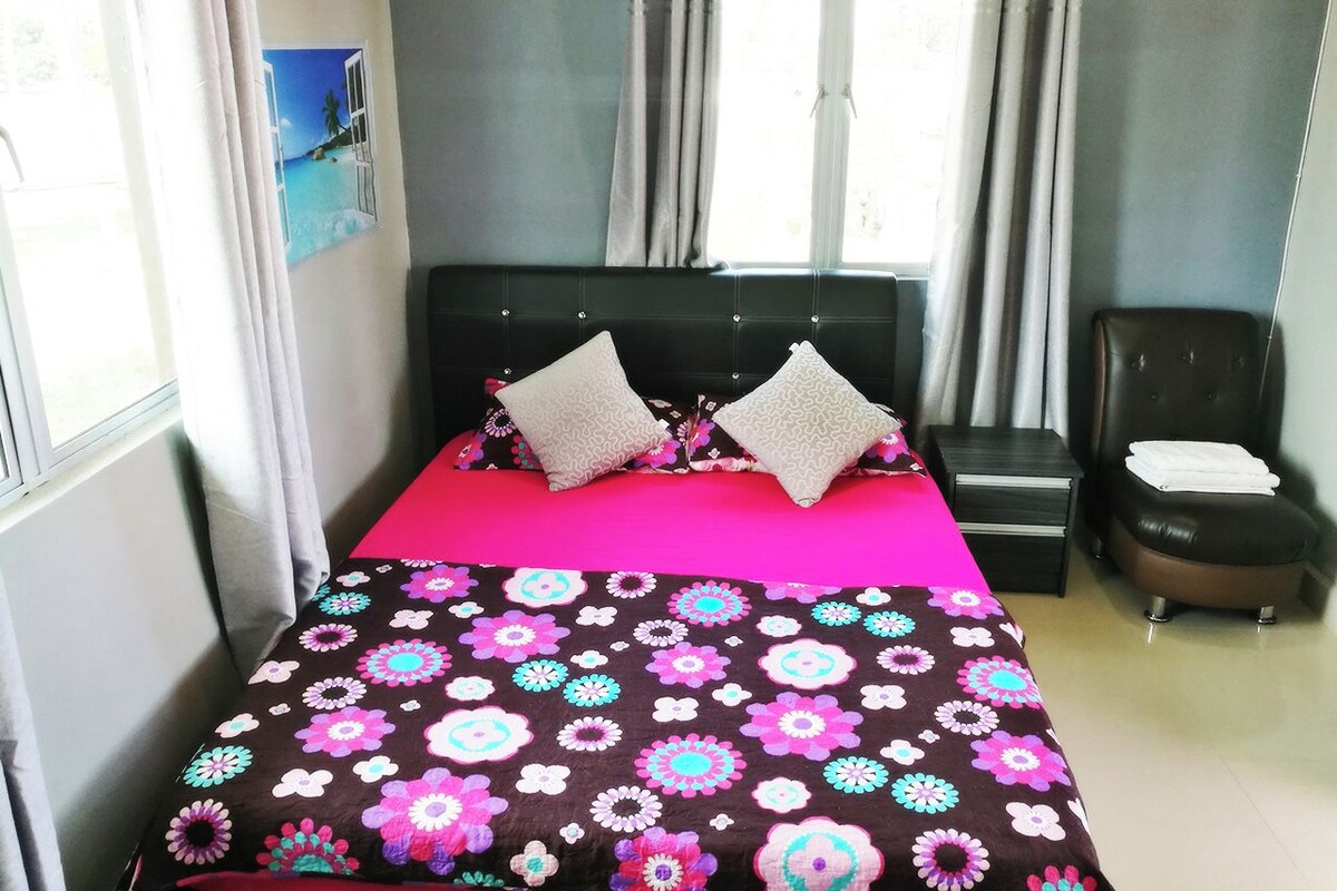A bedroom with a bed, two pillows, a nightstand, a chair, and a window with curtains.