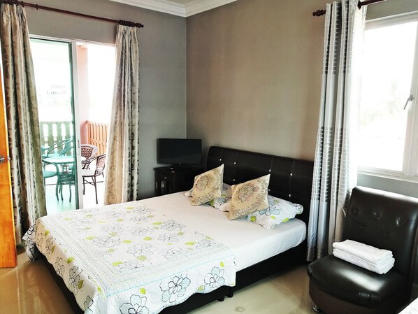 A bedroom with a bed, a TV, a chair, and a balcony with a table and chairs.