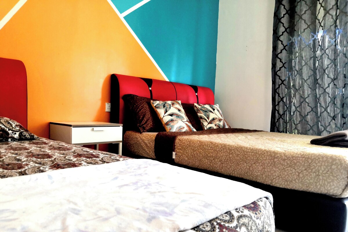 A hotel room with two beds, a nightstand, and a window with patterned curtains.