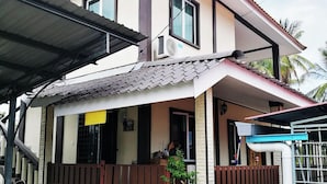 A two-story house with a covered porch, a small garden area with potted plants, and a visible staircase leading to the entrance. - Haji Hassan Guest House (Langkawi)