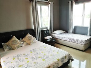 A bedroom with a large bed, a smaller sofa bed, a chair, and a window with curtains.
