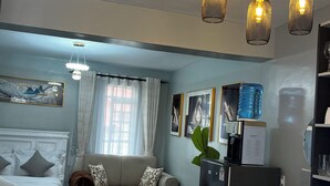 En moderne stue med sofa, sofabord, spiseplads og et køkken med køleskab.