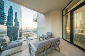 A balcony with a sofa, chairs, and a glass table overlooking a cityscape.