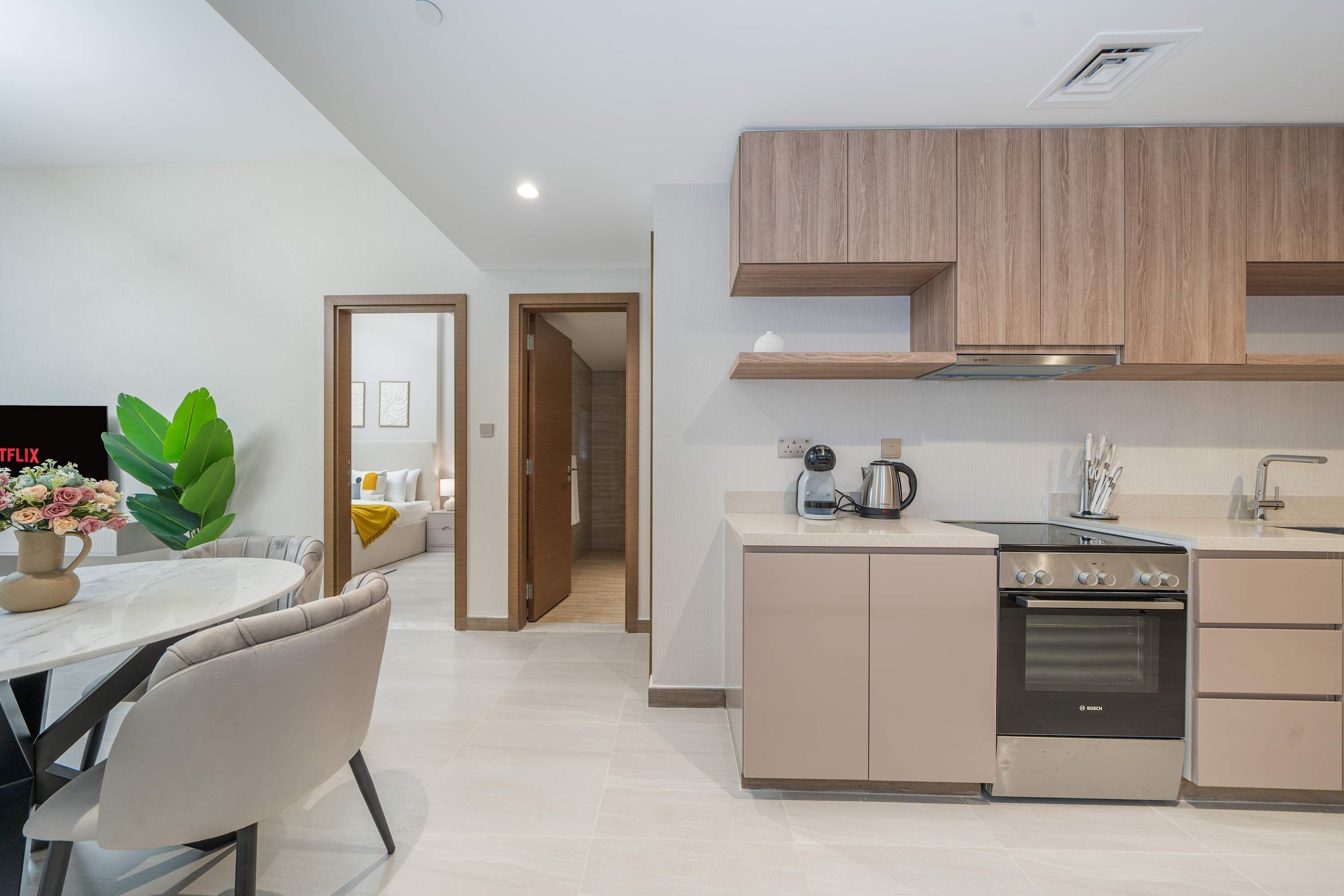 A modern kitchen with a Bosch oven, a dining area with a table and chairs, and a living area with a sofa and a plant.