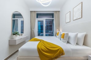 Quarto de hotel moderno com uma cama grande, uma janela com cortinas, uma mesinha com um vaso e vista para a cidade.