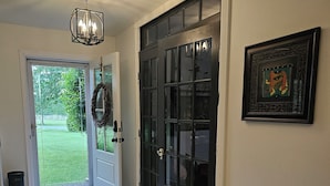 Un pasillo con una puerta negra, una obra de arte enmarco y un accesorio de iluminación.