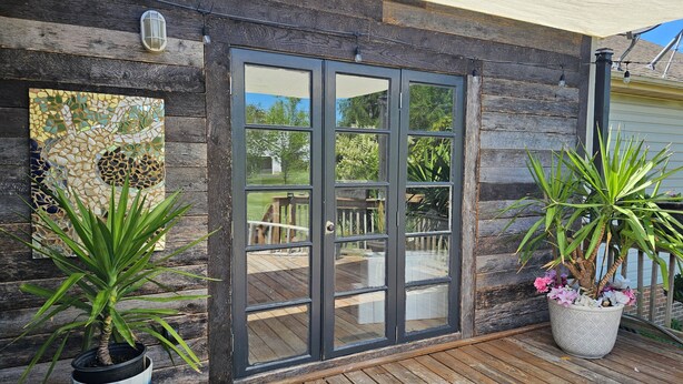 Una terraza de madera con una puerta de vidrio que da a un patio exterior.