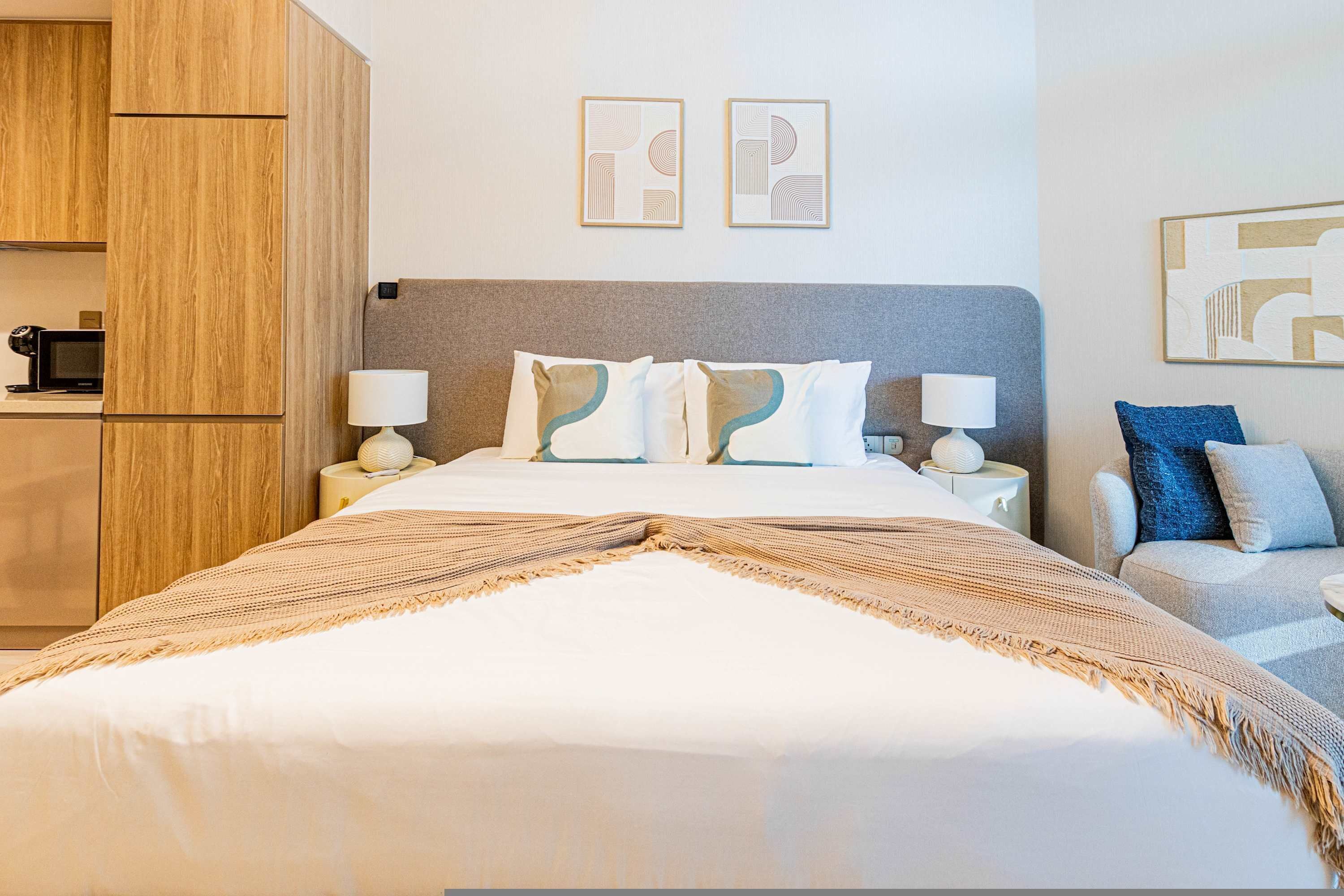 Habitación de hotel ordenada con cama, mesitas de noche, armario y cuadros en las paredes.