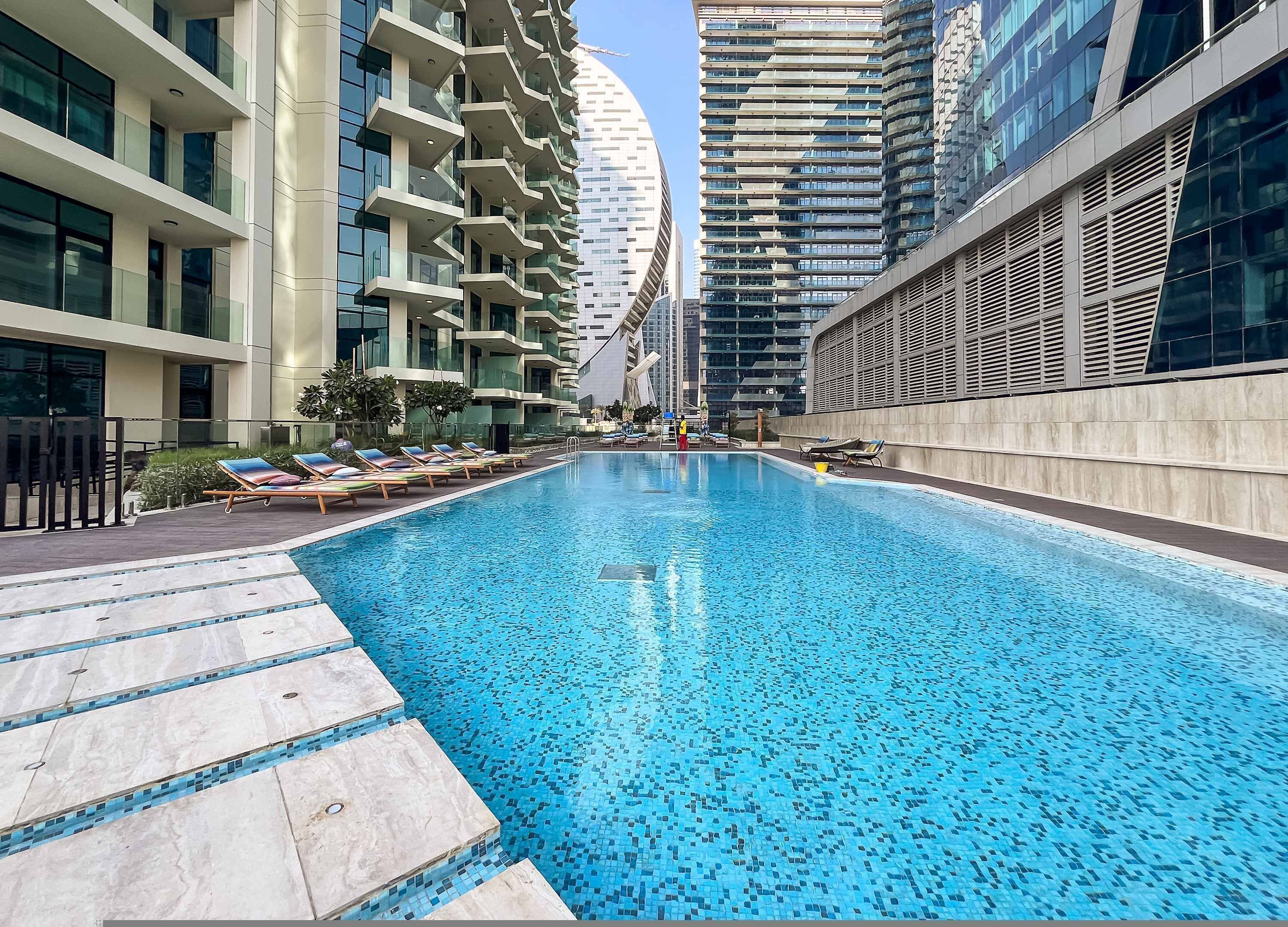 A swimming pool with lounge chairs, surrounded by high-rise buildings.