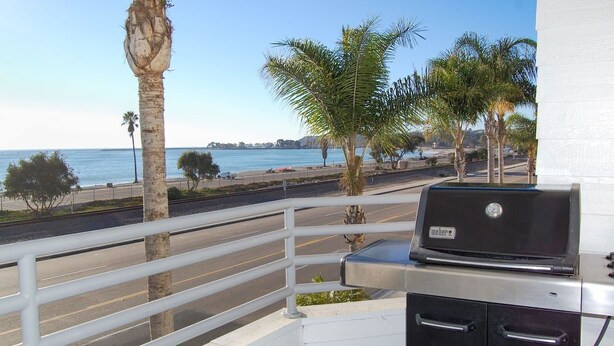 Een balkon met een grill, met uitzicht op een strand met palmbomen en een helder uitzicht over de oceaan.