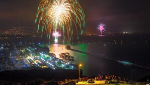 Een nachtzicht van een kuststad met vuurwerk, een brug en een menigte mensen.