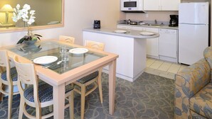 Een kleine keuken met een eethoek, inclusief een tafel met stoelen, een magnetron, een koffiezetapparaat en een koelkast.