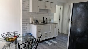 A modern kitchen with white cabinets, a glass table with chairs, and a black refrigerator.